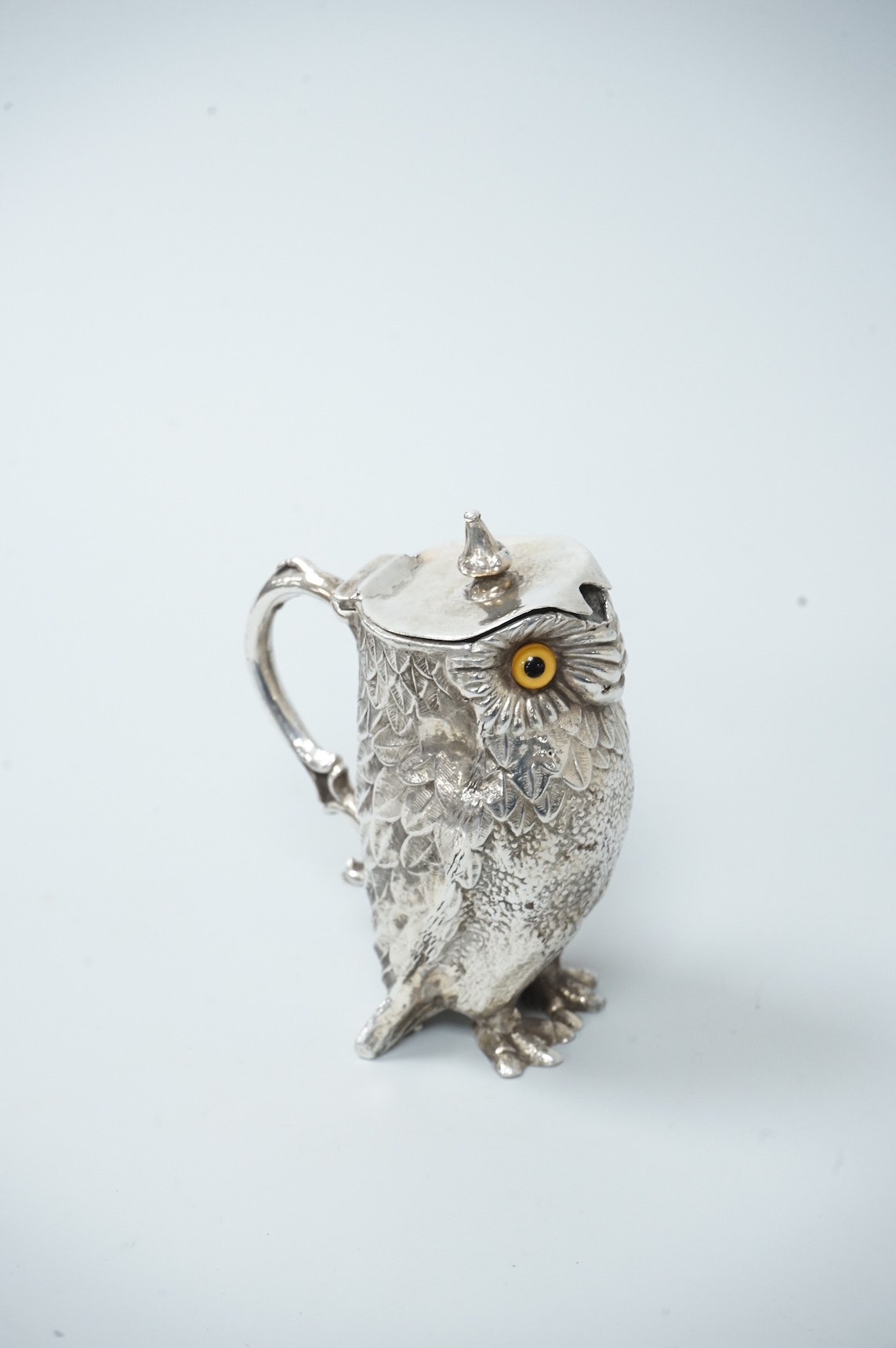 A novelty white metal single handled mustard pot, modelled as a free-standing owl, with hinged cover and textured 'feathers', unmarked, height 95mm.